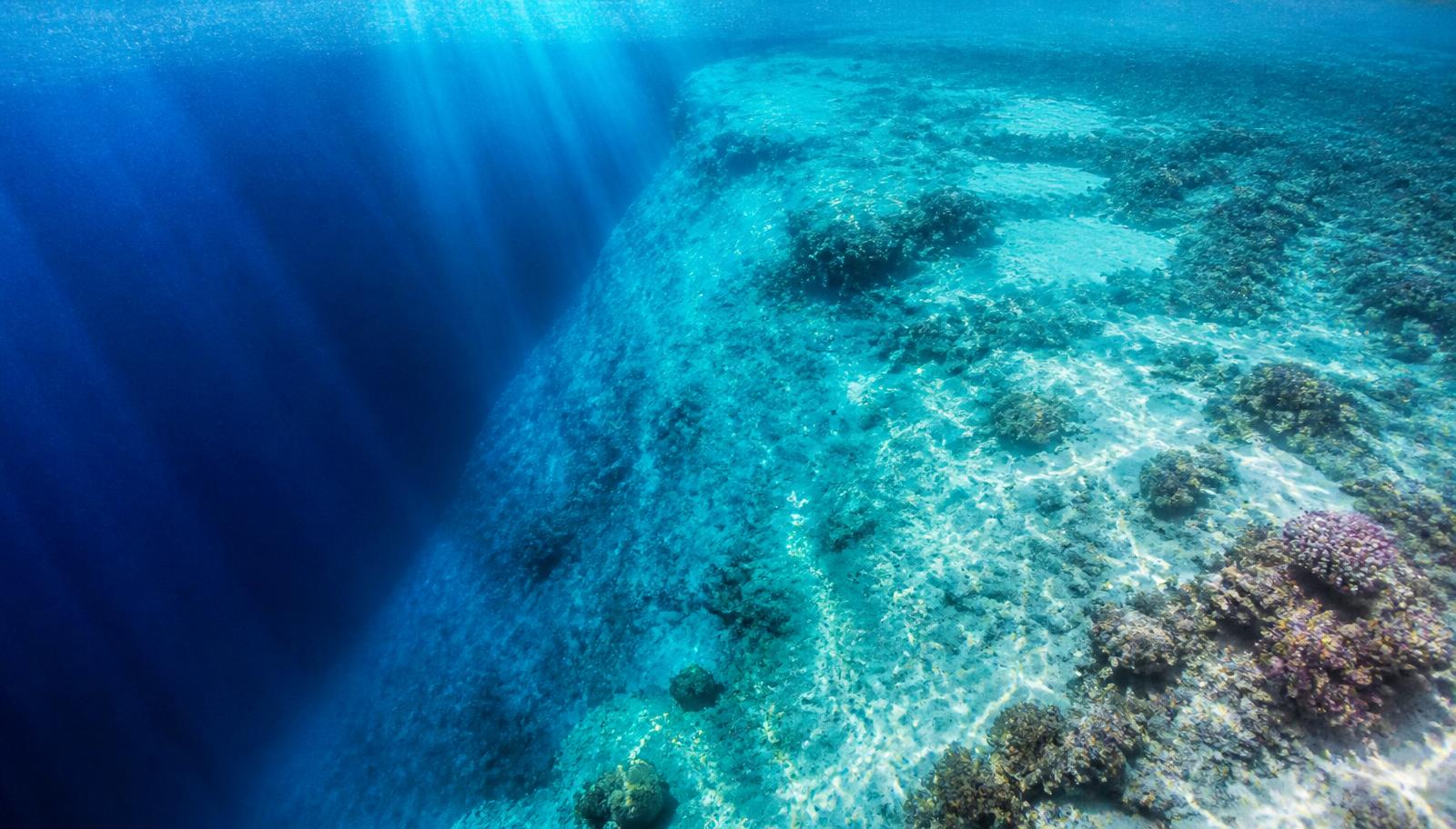 Sunlight through a Maldives lagoon reef dropping into deep blue water